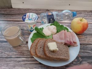 Zdjęcie przedstawia Dietę z ograniczeniem łatwoprzyswajalnych węglowodanów:  Kawa zbożowa z mlekiem Jogurt naturalny Chleb Graham Masło extra Szynka Piastowska- wp., wędzona, parzona z dod. b.sojowego i wody Sałata zielona Woda mineralna 1 szt Jabłko 1 szt Twarożek różany